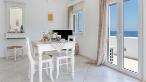 A room with a dining table, chairs, a mirror, and a view of the sea through a sliding glass door. - Apartment 'Sea View Studio' with Sea View, Wi-Fi and Air Conditioning (Astypalaia Town)