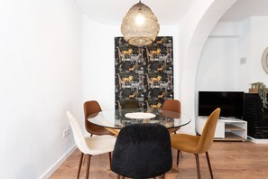 A dining area with a round glass table, four chairs, a black velvet chair, a woven pendant light, and a patterned wallpaper. - Apartment 'Beachside Centre 6pax' with Private Terrace, Wi-Fi and Air Conditioning (Fuengirola)