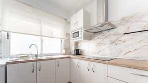 Eine moderne Küche mit weißen Schränken, einer Marmor-Spritzschutzwand, einer Mikrowelle und einem Fenster.