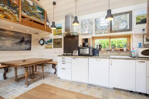 Una cucina con mobili bianchi, un tavolo di legno, un forno a microonde e diversi elettrodomestici.