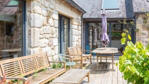 A stone building with a wooden deck, outdoor seating, and a table with an umbrella.
