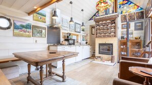 A rustic kitchen with a wooden table, hanging lights, and a fireplace.