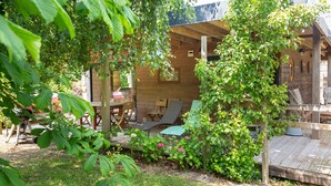 Una cabaña de madera con terraza, rodeada de exuberante follaje y un pequeño jardín.