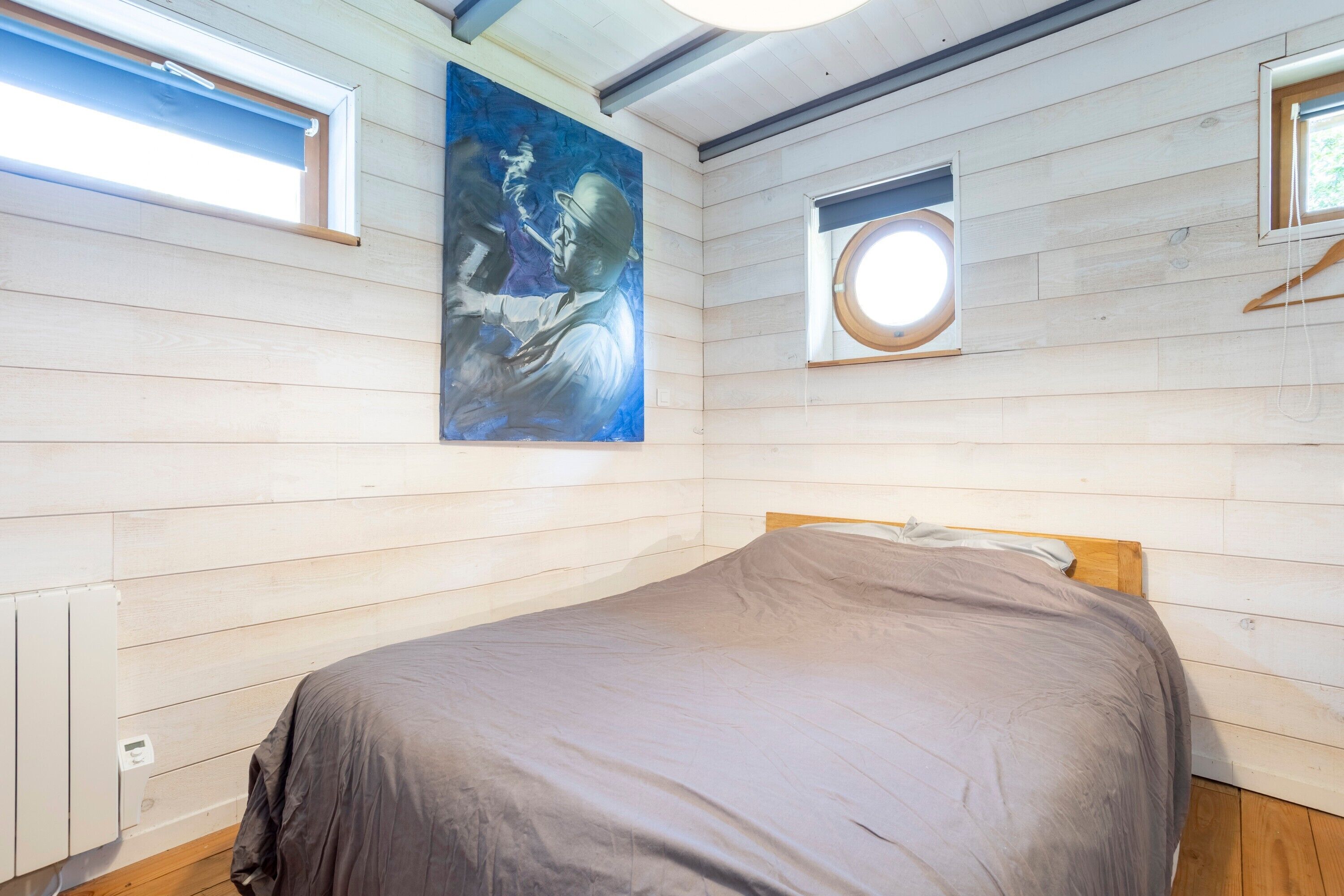 Une chambre à coucher avec un lit, un tableau et deux fenêtres.