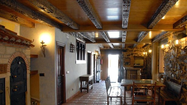 A rustic interior with a stone fireplace, wooden beams, and a tiled floor.