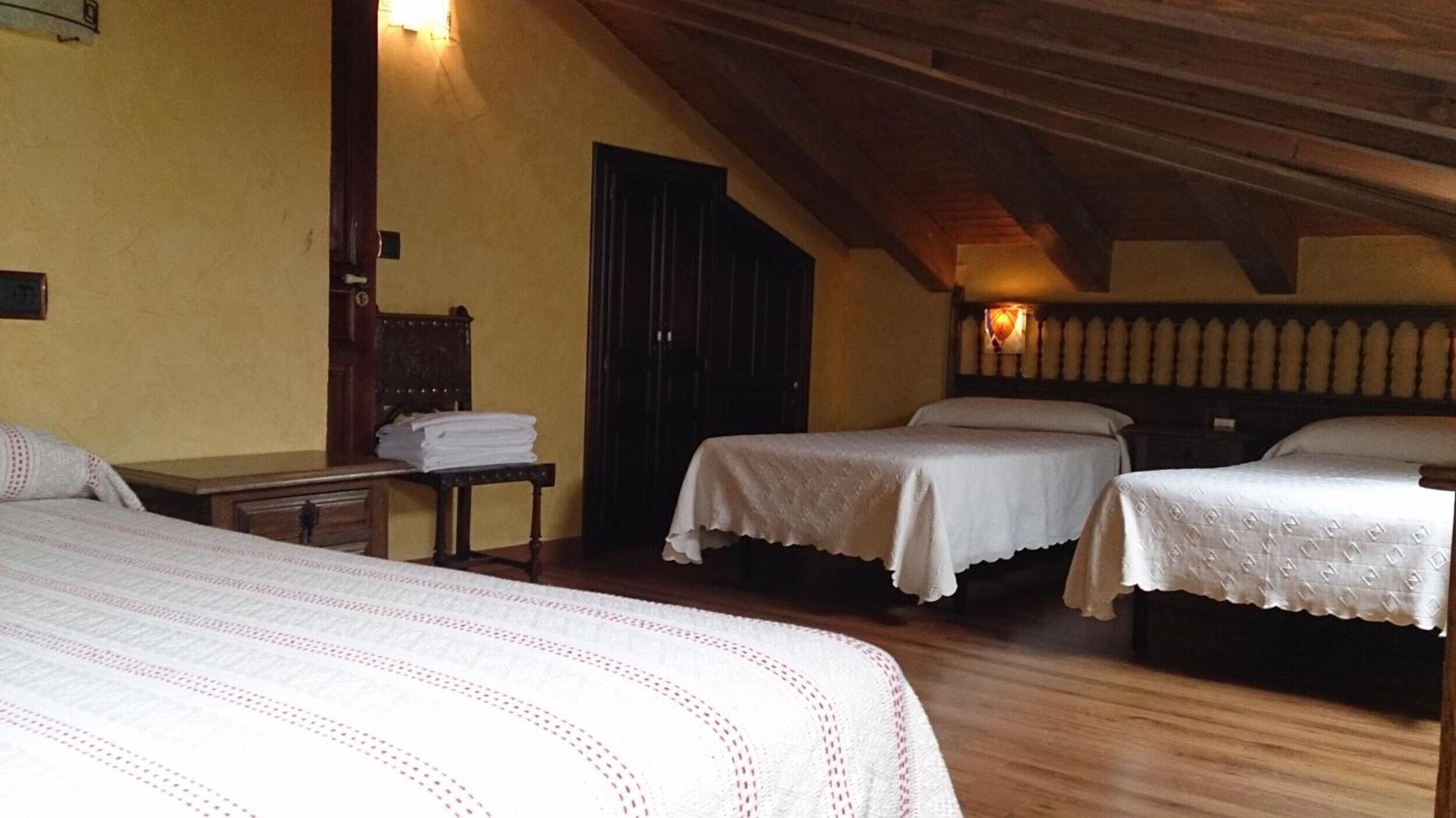 A room with two beds, a wooden ceiling, a door, and a small table with folded towels.