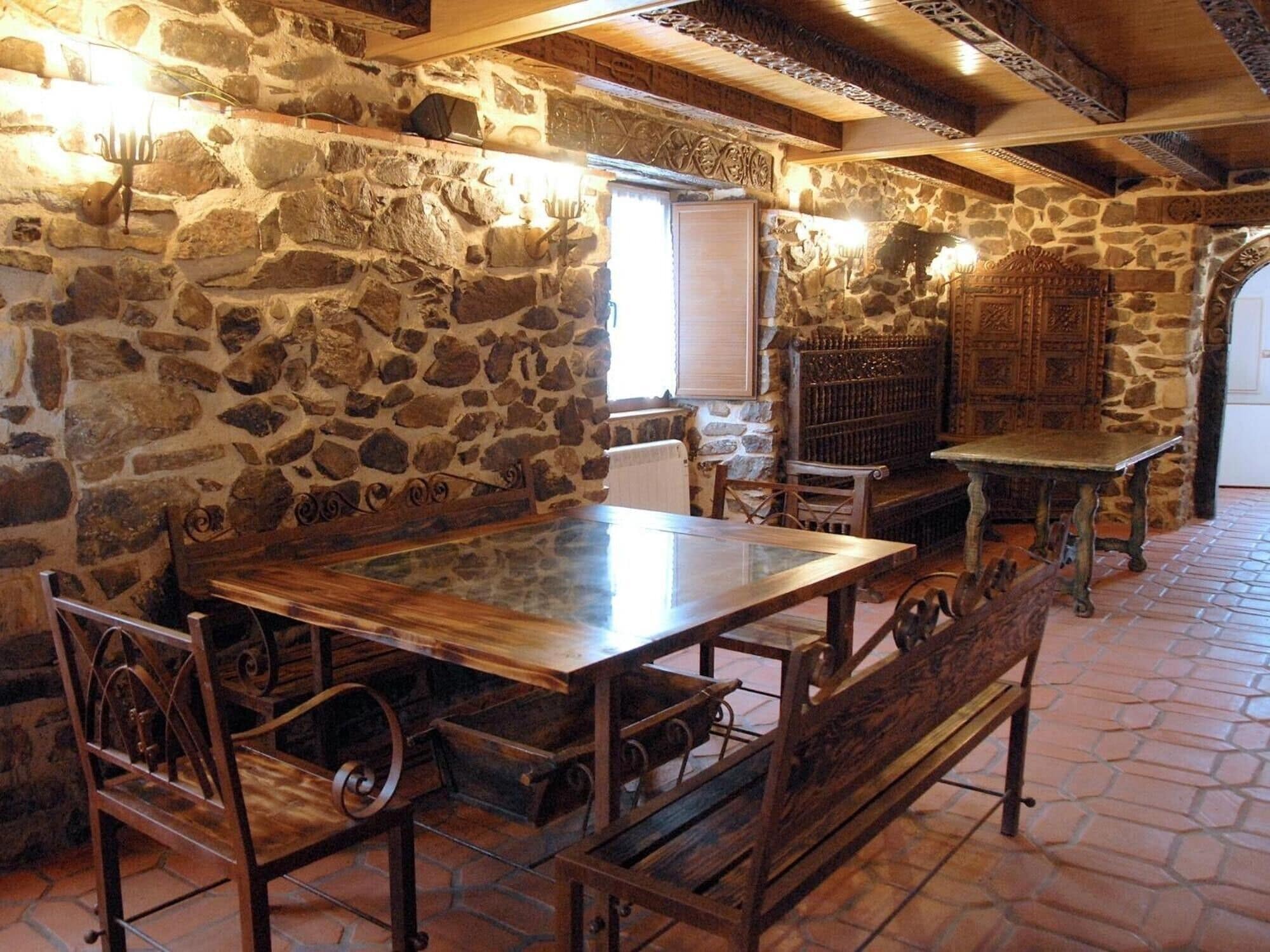 Une pièce rustique aux murs de pierre, avec une table et des bancs en bois, une cheminée et un buffet en bois.