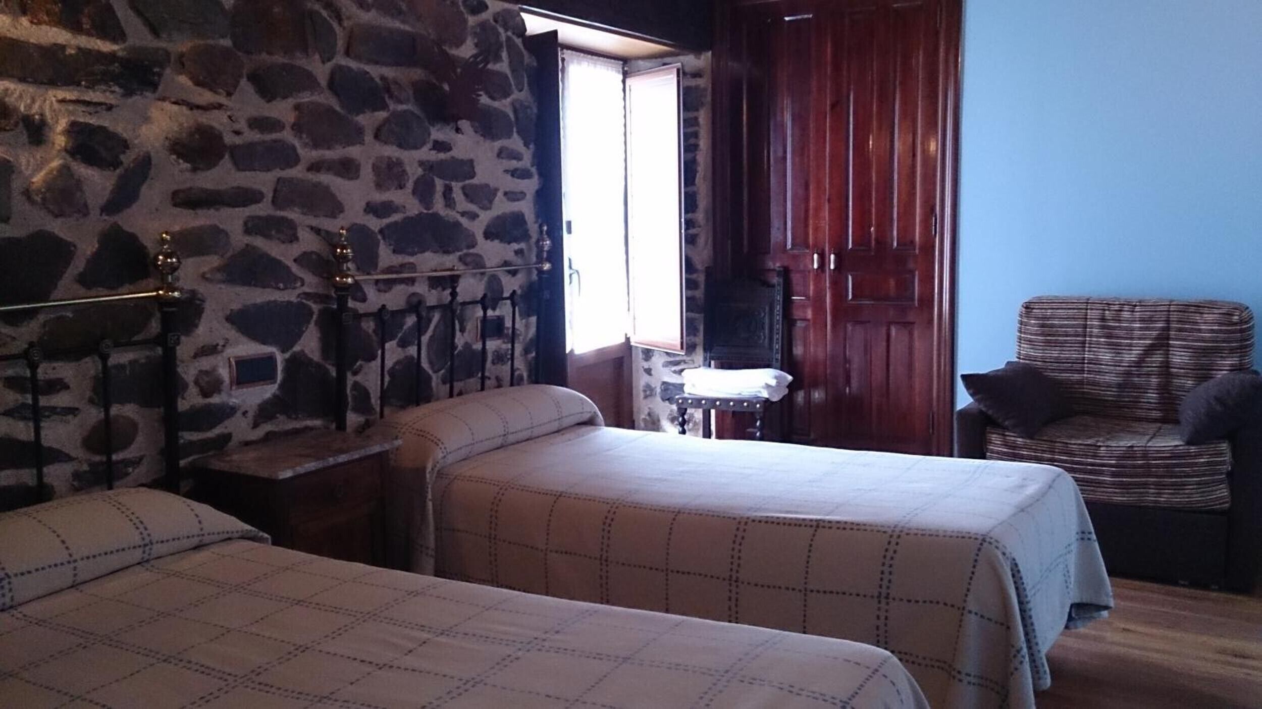 A room with two beds, a stone wall, a wooden door, and a chair.