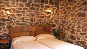 A room with a stone wall, a wooden bed with two pillows, and two wall-mounted lights.