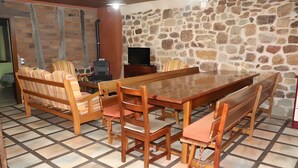 Un comedor con mesa y sillas de madera, televisor y pared de piedra.