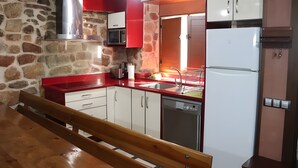 Una cocina con paredes de piedra, un banco de madera, un refrigerador blanco y una encimera roja.