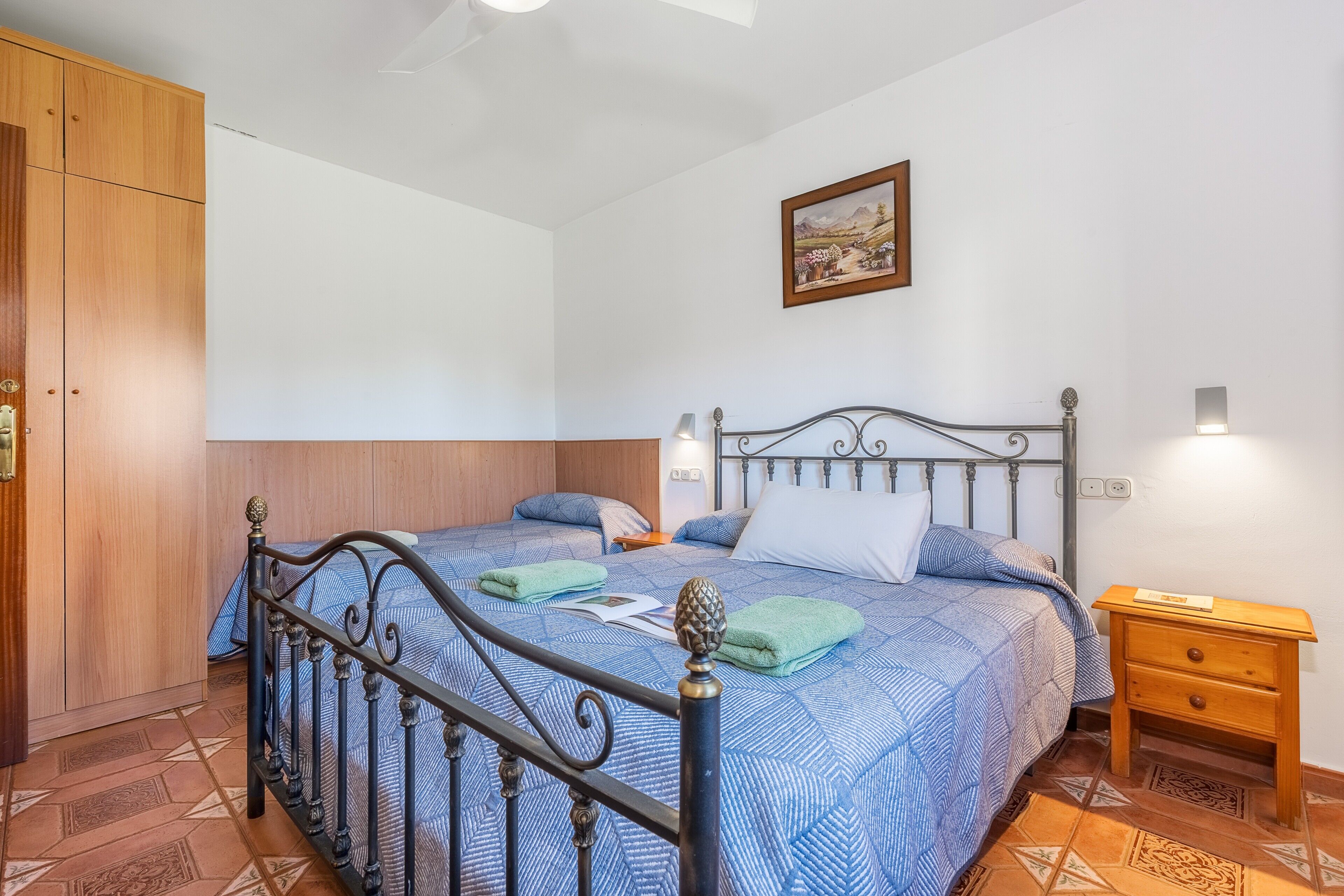 Un dormitorio con cama, armario de madera, mesita de noche y un cuadro en la pared.