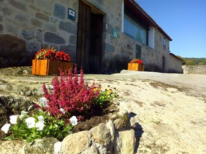 Ein Steinhäuschen mit einer Holztür, Blumenkästen mit roten Blumen und einem blauen Himmel.