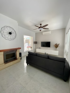 A modern living room with a fireplace, a black sofa, a TV mounted on the wall, and a ceiling fan.