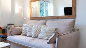 Ein beiges Sofa mit gemusterten Kissen, ein runder Tisch und ein großer Spiegel an der Wand.