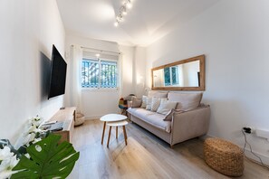 A modern living room with a sofa, a flat-screen TV, a coffee table, and a large plant.