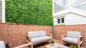 Eine Terrasse mit grüner Wand, zwei weißen Sofas, einem Holztisch und einem Blumentopf.
