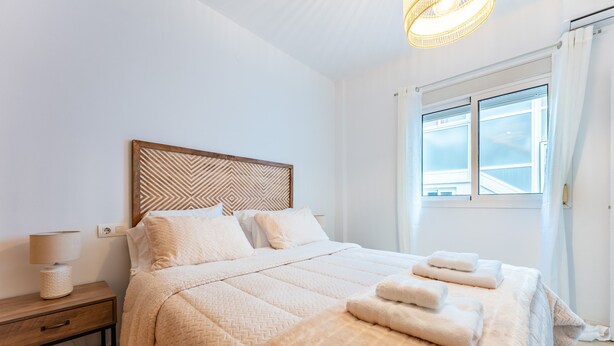 Ein Schlafzimmer mit einem Bett, einem Nachttisch, einer Lampe und einem Fenster mit Vorhängen.