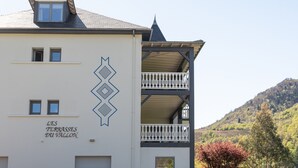 Un edificio con un letrero que dice 'LES TERRASSES DU VALLON', balcones y un paisaje montañoso de fondo.