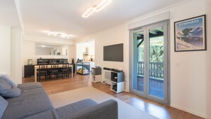 Una sala de estar moderna con un sofá, un televisor de pantalla plana, un comedor y un ventanal corredizo que da a un balcón.