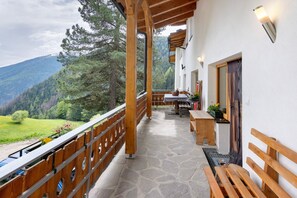 A wooden balcony with stone flooring, a wooden table, and benches.