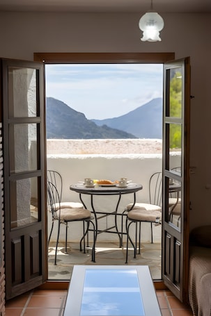 An open door leading to a balcony with a table and chairs, a bed, and a view of mountains.