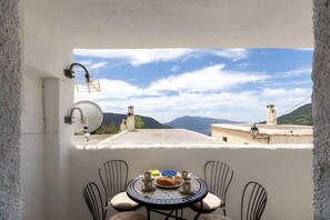 Un balcon avec une table dressée pour deux personnes, une antenne parabolique et une vue sur des montagnes lointaines.