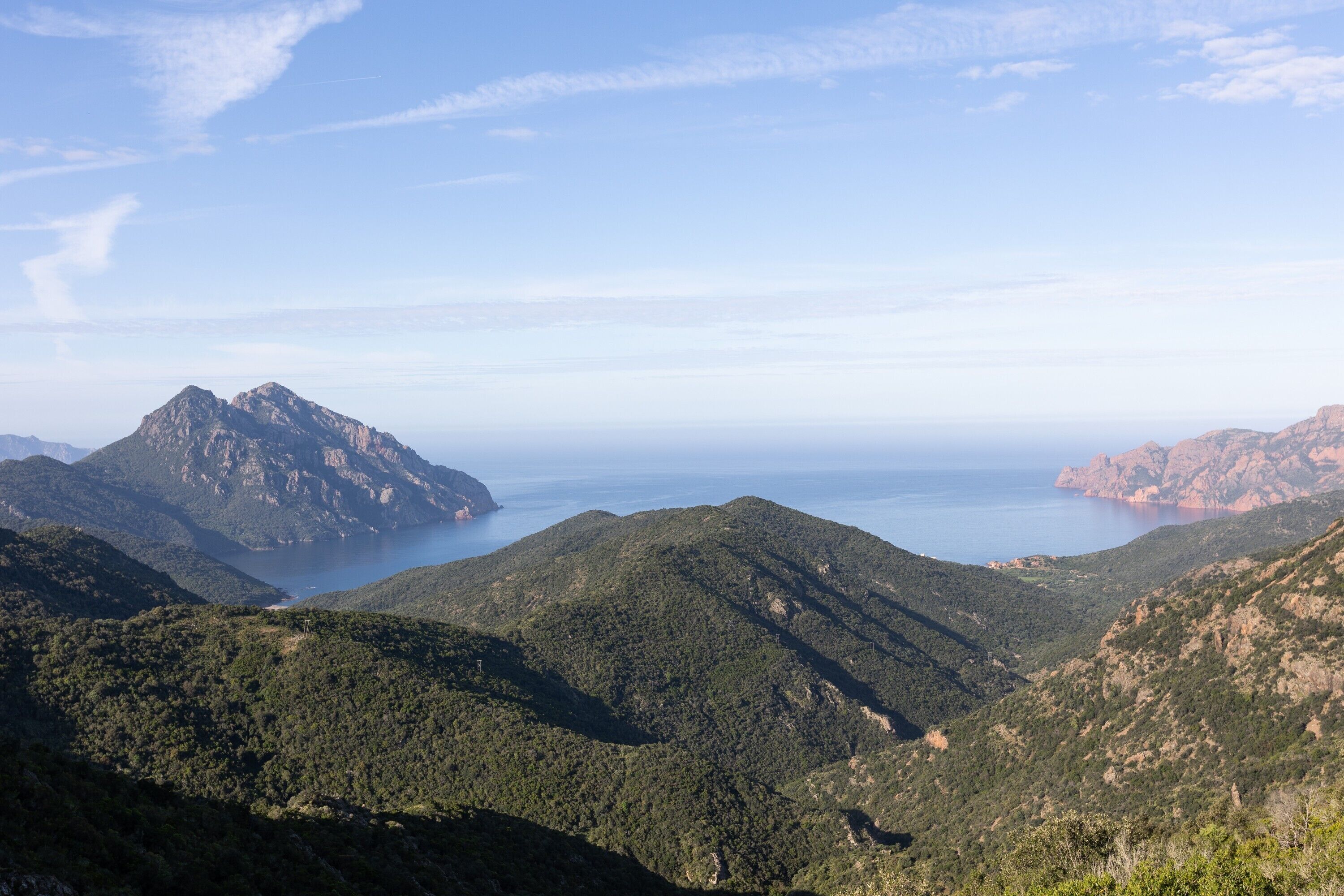 Eine gebirgige Landschaft mit freiem Blick auf das Meer und entfernte Felsenformationen.