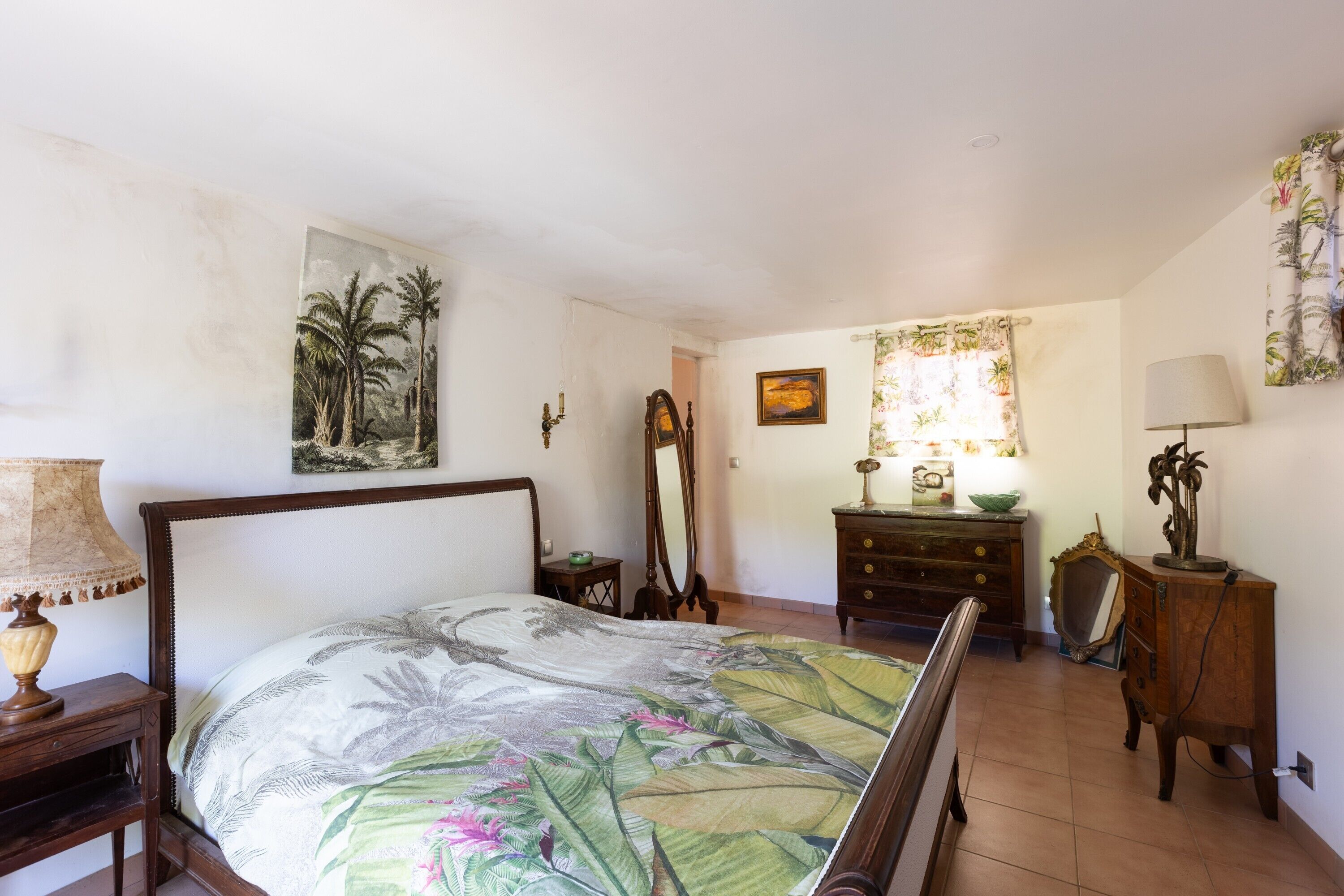 Een slaapkamer met een bed, een ladekast, een spiegel en een schilderij aan de muur.