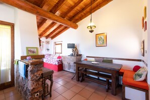 A rustic interior with a stone wall, wooden ceiling beams, a dining table, and a bench.