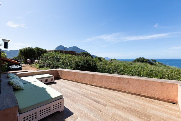 Eine Dachterrasse mit Blick auf das Meer und die Berge, ausgestattet mit einer Sitzecke und Kissen.