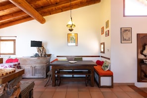 A rustic kitchen with wooden beams, a dining table with benches, and a hanging light fixture.