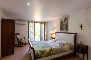 Ein Schlafzimmer mit einem Bett, einem Schaukelstuhl, einem Nachttisch mit Lampe und einem Wandbild.