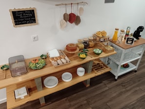 Um buffet de café da manhã com diversos alimentos, uma lousa com mensagens de boas-vindas e decorações penduradas.