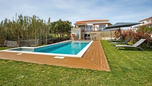 A swimming pool with a wooden deck, lounge chairs, and a house in the background. - Studio 'Quinta Dos Raposos - Villa Terra' with Shared Pool, Terrace and Wi-Fi (Nazaré)