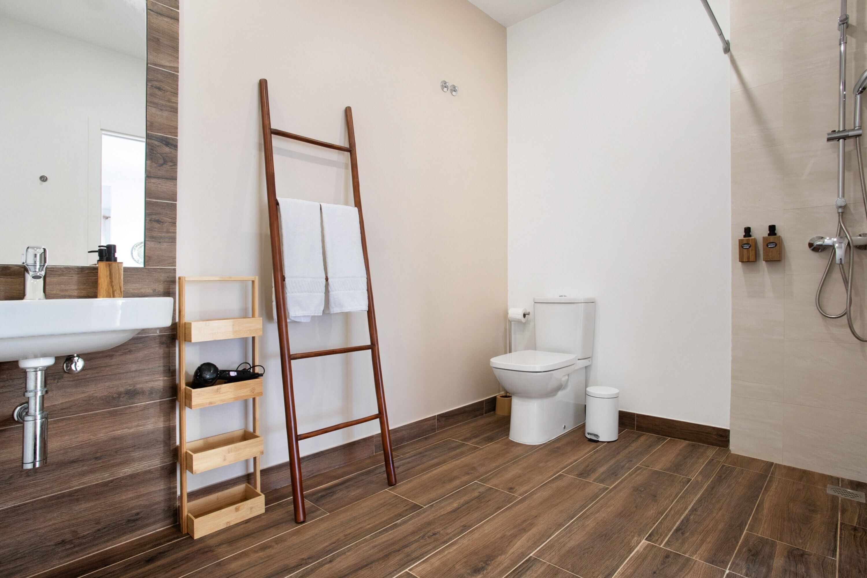 Une salle de bain avec une échelle en bois, des toilettes blanches, un lavabo et une douche.