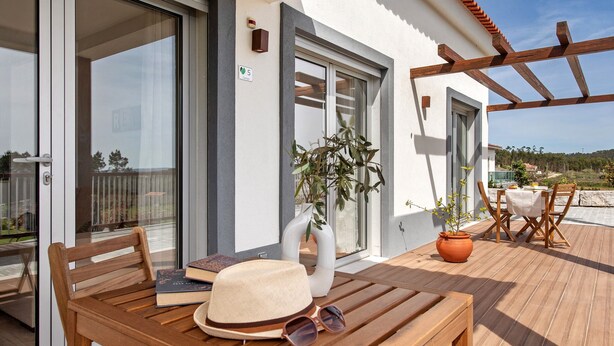 A wooden table with a hat and sunglasses, a white vase with a plant, and a wooden chair on an outdoor patio. - Country House "Quinta dos Raposos" - Villa Mar (Nazaré)