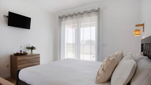 A bedroom with a bed, a flat-screen TV, a bedside table with a plant, and a window with curtains. - Country House "Quinta dos Raposos" - Villa Mar (Nazaré)