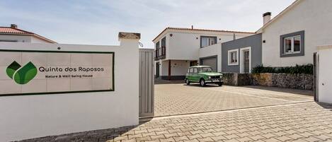 A gated entrance to Quinta dos Raposos Nature & Well-being House with a paved driveway and a parked car.