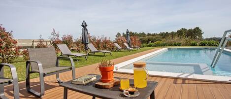 A poolside area with lounge chairs, a table with drinks, and a view of the pool.
