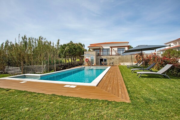 Une piscine avec une terrasse en bois, des chaises longues et une maison en arrière-plan.