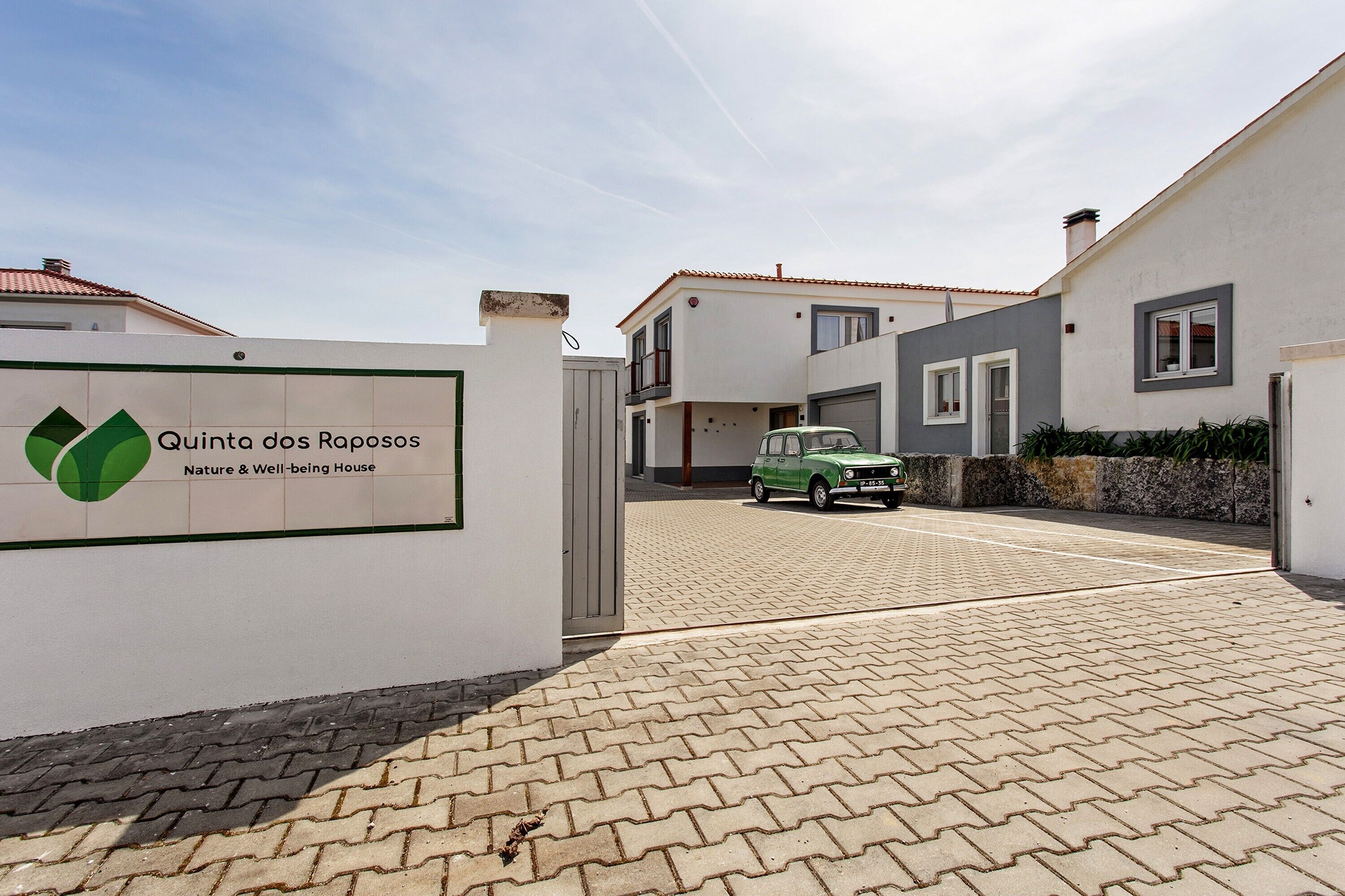 A gated entrance to Quinta dos Raposos Nature & Well-being House with a paved driveway and a parked car.