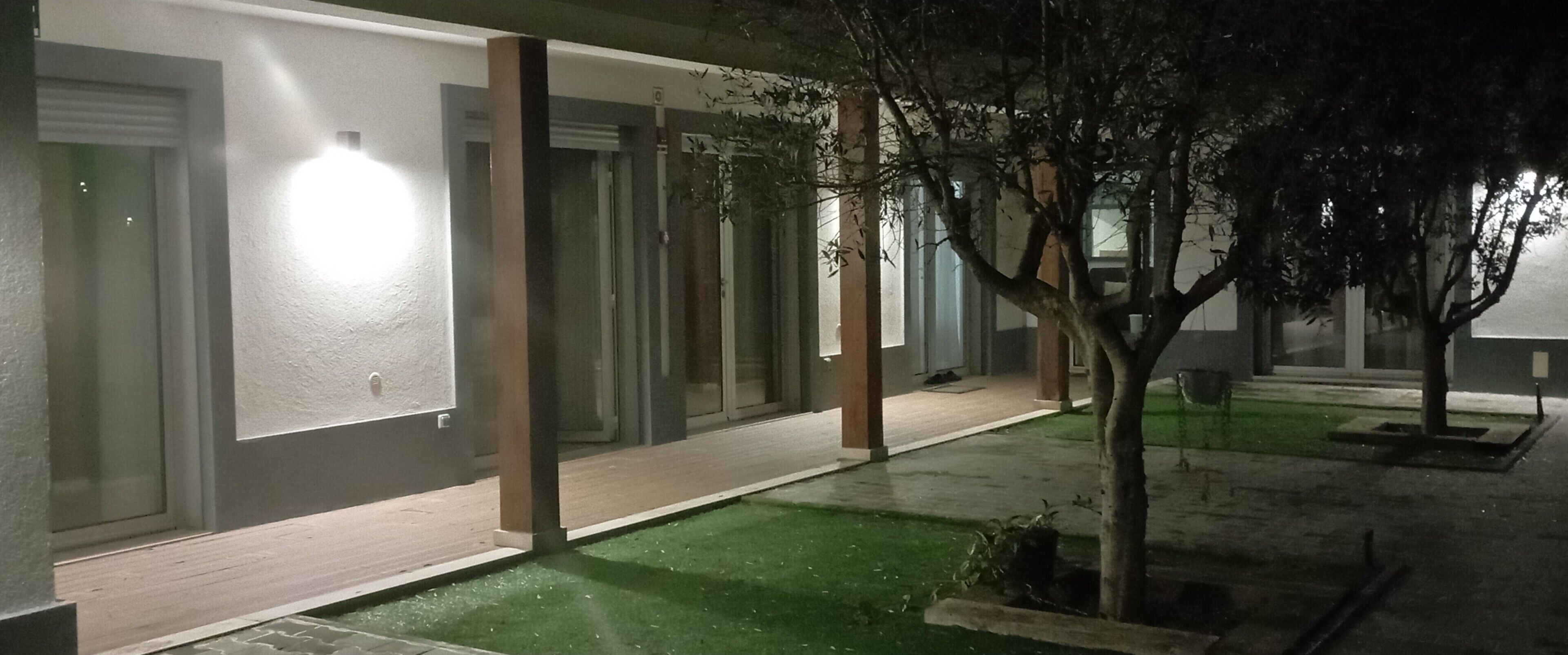 A building with a covered outdoor area, a green lawn, and a tree.