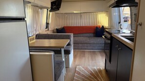 Ein kompaktes Wohnmobil-Interieur mit Küchenzeile, Essbereich und Sitzgruppe inklusive Sofa und Kissen.