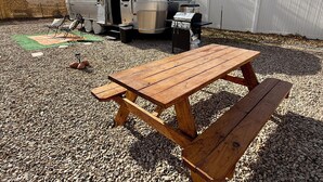 Ein Holztisch mit Bänken auf Kies, ein silberner Wohnmobil und ein Grill.