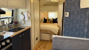 Ein kompaktes Wohnmobil-Interieur mit Küchenzeile, einem Bett mit gemustertem Kopfteil und einem grauen Sofa.