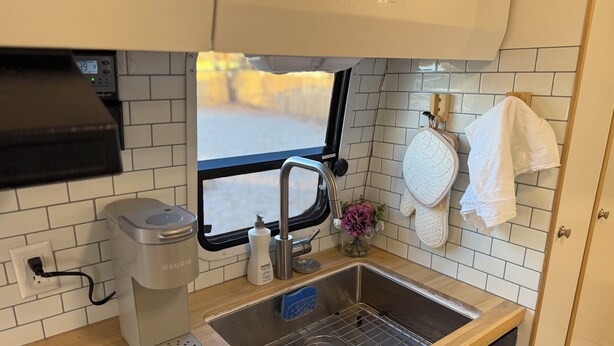 Eine kleine Küche mit Kaffeemaschine, Spüle und einem Fenster mit Blick auf eine verschneite Landschaft.