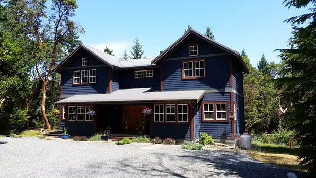 A two-story house with a front porch, multiple windows, and a gravel driveway.