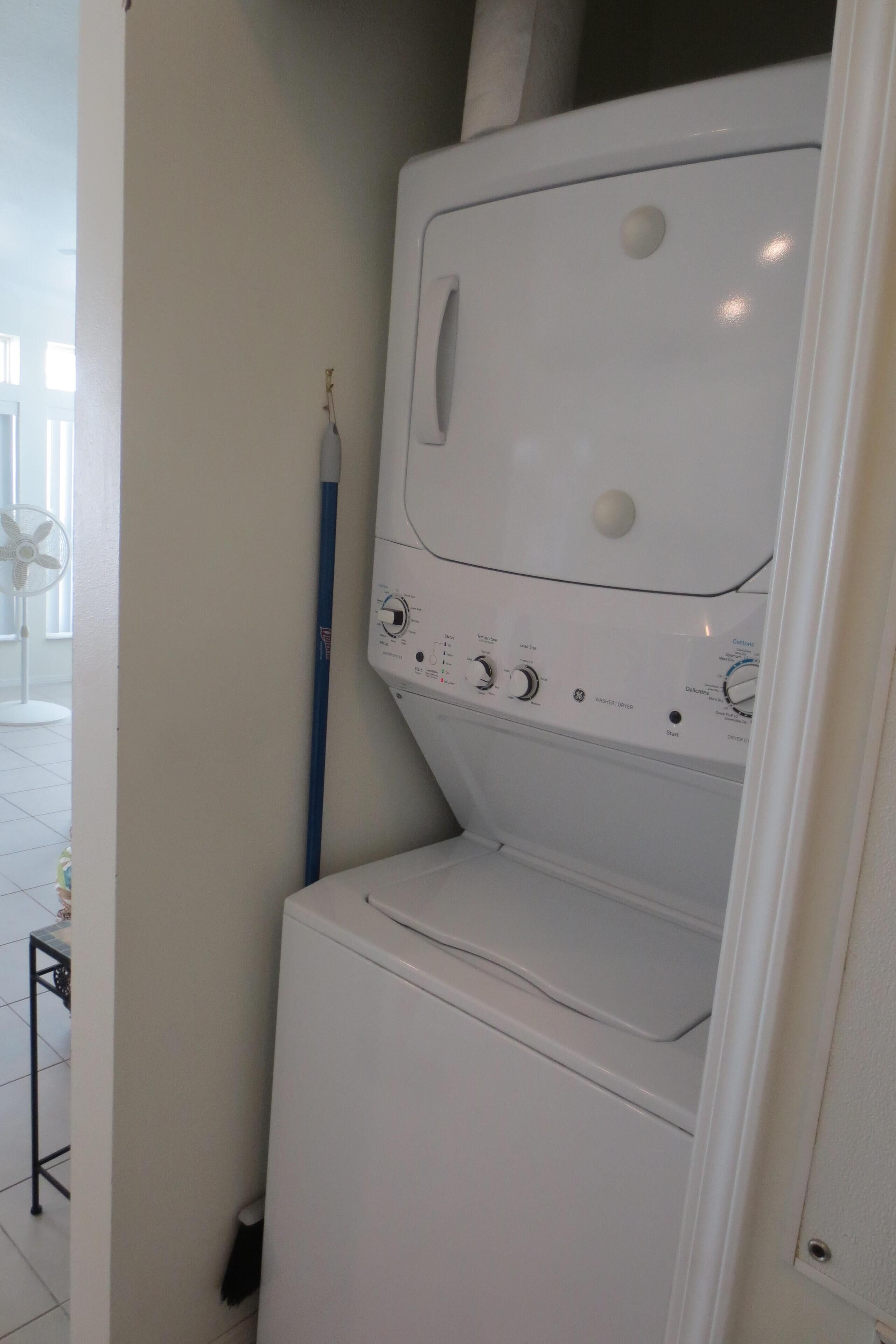 A compact, white washing machine in a small laundry room with a visible control panel and a blue pole.