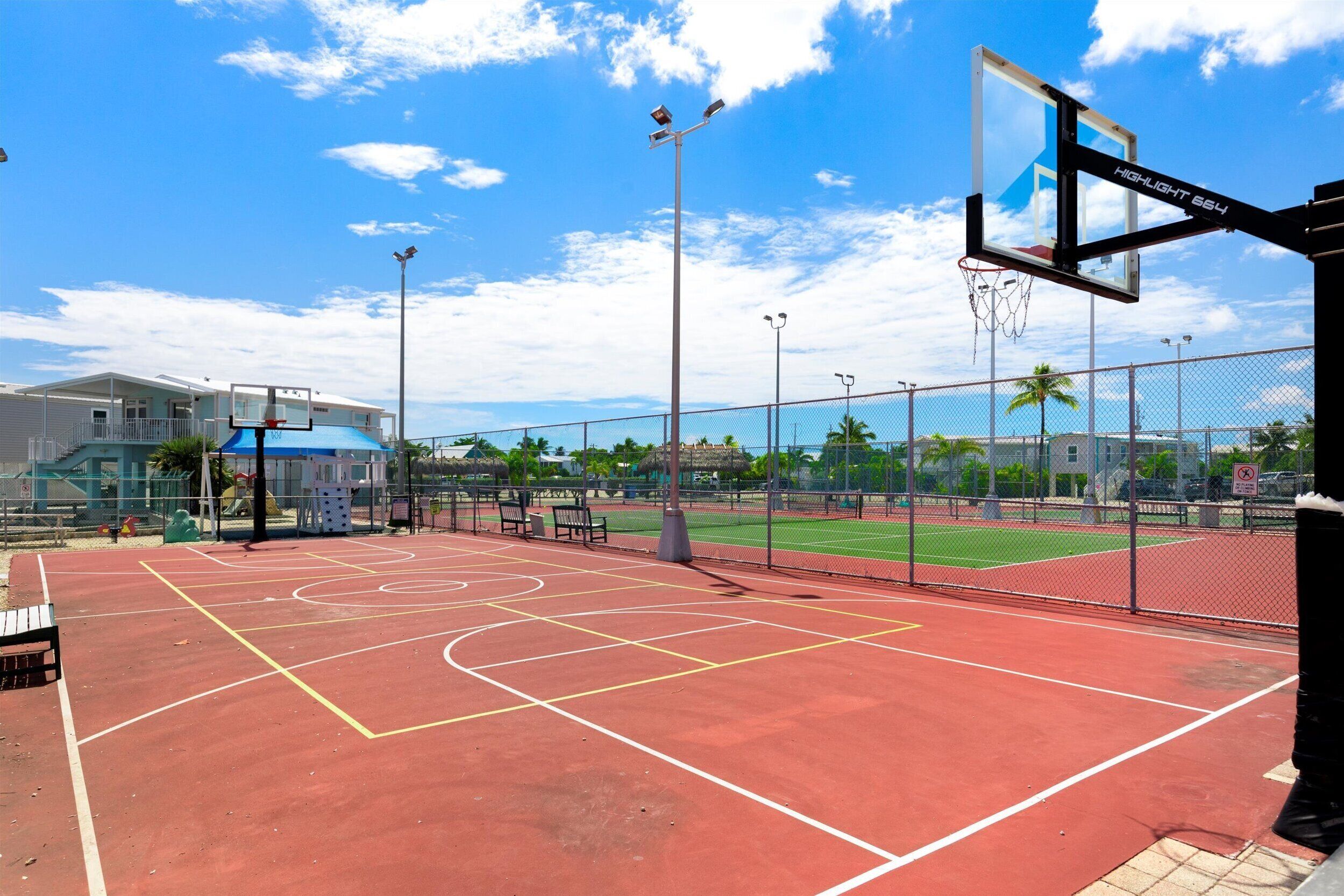 Un terrain de basket en plein air avec une surface rouge, un panier de basket et une clôture en treillis métallique.